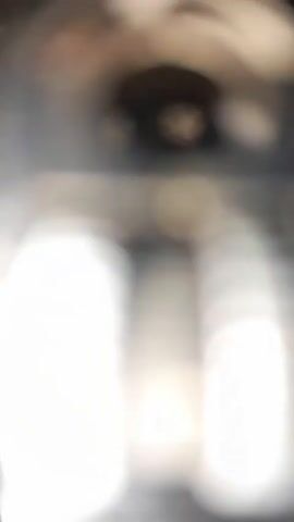 The camera focuses on a metallic lighter lying on a mottled brown surface. The top portion of the lighter, including the flint wheel, is visible. The surface appears to be concrete with a pattern of cracks. The lighting is relatively bright, causing glare on the lighter's surface and casting a dark shadow to its right. The video transitions from blurry to a clearer focus on the object.