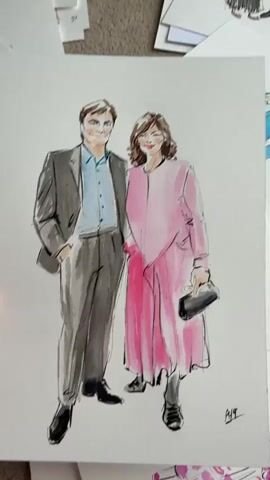 A hand holds up a drawing of a man and a woman. The man is wearing a gray suit, light blue shirt, and black shoes. The woman is wearing a long pink dress with black shoes and holding a black clutch purse. There are other drawings on the floor around the drawing that is being held up. A voice announces that the person is a life event illustrator.