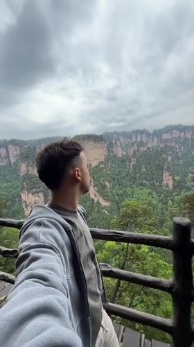 Tourist photographs scenic mountain views from wooden platform in Luoguta
