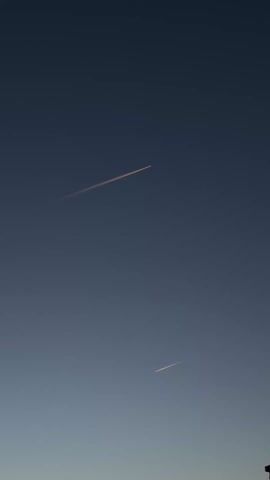 The video depicts two contrails in a darkening, cloudless, blue sky.  The contrails are white and thin, and run from the upper left to the bottom right. The lower contrail is shorter.