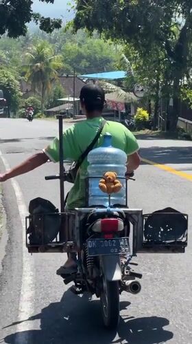 Motorcyclist carries water jug on rural Indonesian road