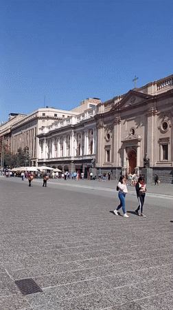 Pedestrians gather at ornate cathedral in Santiago city square