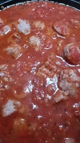 The video shows a close-up of a frying pan filled with tomato sauce and meatballs. The meatballs appear to be a light color. The sauce is thick and has a bright red color. Some pieces of onion are also visible in the sauce. The pan is sitting on a stovetop.