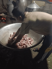 Person prepares raw meat over fire pit with containers