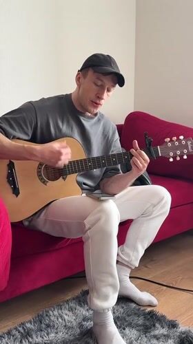 Man performs acoustic guitar session on red couch in Murino