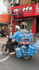 Motorcyclists navigate Thủ Đức streets, one hauling water bottles