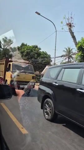 A yellow Mitsubishi dump truck with wooden sides is seen driving on a road. A white Toyota Avanza is seen driving on the road. A black car is seen driving on the road. A tan Honda City is seen driving on the road. A blue and white Hino dump truck is seen driving on the road.