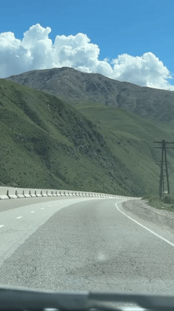 Vehicle travels mountain road in sunny Cholok, Kyrgyzstan