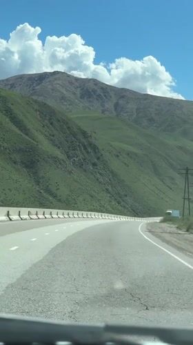 Vehicle travels mountain road in sunny Cholok, Kyrgyzstan