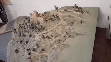 Medieval museum exhibit with castle diorama, swords, and silver coins