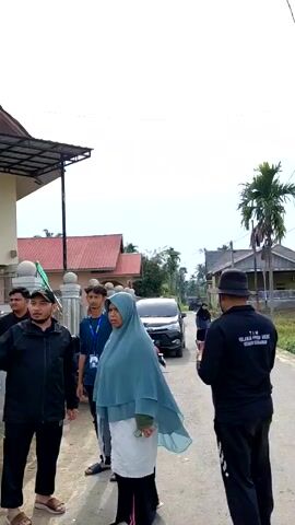 The video shows a group of people standing in a residential area. Some of them are talking and gesturing. In the background, there are houses, vehicles, and palm trees. Some people are wearing headscarves. There is a mosque visible in one shot. The weather appears to be overcast. The video appears to be taken during the day.