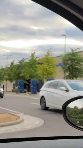 The video begins with a close-up of the front of a white Hyundai i40 parked in front of a building. The car has its headlights on and the license plate is visible. The camera then pans to the left, revealing a sign for Leclerc, a French supermarket chain, and an electric vehicle charging station. The camera continues to pan, showing more of the Leclerc building and a black utility structure. Finally, the video shows the interior of a Fiat 500, with a hand on the steering wheel, as the car drives past the Leclerc building. The sky is cloudy throughout the video.