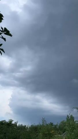 The video shows a time-lapse of dark, ominous storm clouds gathering over a lush green landscape. The clouds are dense and appear to be moving quickly across the sky. The overall mood is one of an approaching storm.