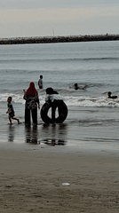 Beach day in Lhokseumawe with swimmers, kids, and a cargo ship offshore
