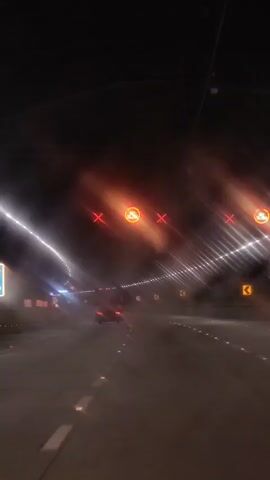 A video shows a dark tunnel with lights on the walls. There are several red Xs and a circular sign with the words GO SLOW in white letters against an orange background. A car is visible driving away from the camera. The camera appears to be inside a vehicle.