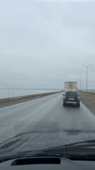 Motorist drives past lake on wet road in Chaikovsky