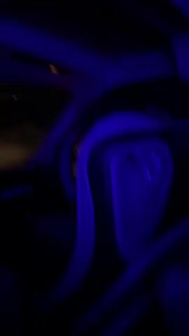 The video shows a group of people inside a vehicle illuminated by blue lights. The camera is moving, and the footage is blurry, suggesting the vehicle is in motion. People are visible in the seats, some with their hands raised or hair being pushed back, indicating movement or excitement. The overall atmosphere appears to be dark with intermittent blue lighting.