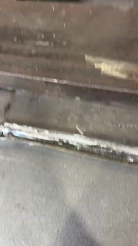 The video shows a close-up view of a metal surface with a visible weld seam. The weld is located horizontally across the frame, appearing to join two pieces of metal. The surface is dark and appears to be industrial in nature. There is some discoloration and texture on the metal, suggesting it may be aged or used. The lighting is somewhat dim, and the camera is focused on the weld area. The footage appears to be from a mobile device, with slight camera shake.