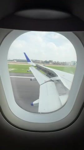 The video begins with a view from an airplane window, showing the wing and runway as the plane is taxiing. The camera pans across the wing and then shows the interior of the plane, focusing on a passenger's legs and the seat in front of them. The video ends with a similar view to the beginning.