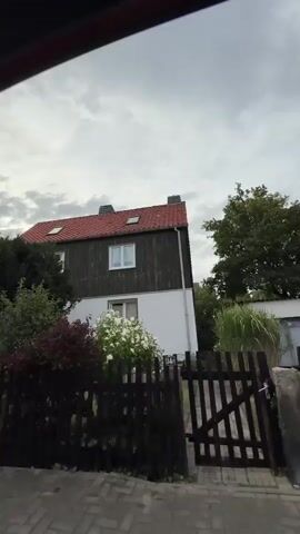 The video shows a residential street with houses and trees. The camera pans across the scene, showing different houses and vegetation. The sky is cloudy.