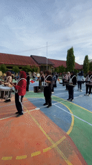 Marching band rehearses drumline and flag routines on outdoor court