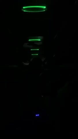 The video shows a dark interior, possibly a limousine, with green neon lights on the ceiling. The lights are arranged in a descending pattern, starting with a ring, then a horizontal bar, and finally smaller bars. A small blue light is visible on the floor. The silhouettes of people can be seen in the background. Upbeat music is playing.