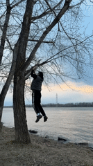 Man exercises on tree branch by water in Chaikovsky