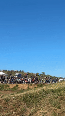 Large crowd gathers on hillside with tents and vehicles