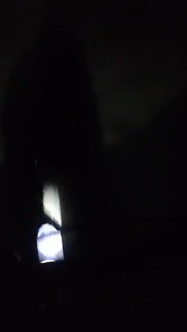 The video shows a dark environment with a bright light source being moved. The light casts a large, undefined shadow on the background. The light source appears to be a small, possibly handheld device. The movement of the light source is jerky and uneven. No people or specific objects besides the light source and its shadow are clearly visible. The environment is otherwise completely dark.