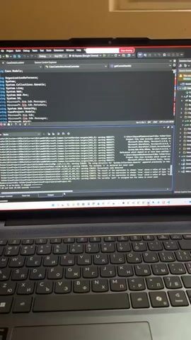 The video shows a desk with a laptop and a monitor. The laptop screen displays lines of code, likely programming or software development. The monitor shows a "Payment Reminder" email from "BORING POLARIS INDUSTRIES," detailing property information and a "Statement Closing Date" of "08-30-2023." A hand is visible using a mouse, interacting with the screen. Various objects are scattered on the desk, including a radiator, a blue basket, a pack of cigarettes, a small bottle, and several rubber ducks. The environment appears to be an indoor workspace.