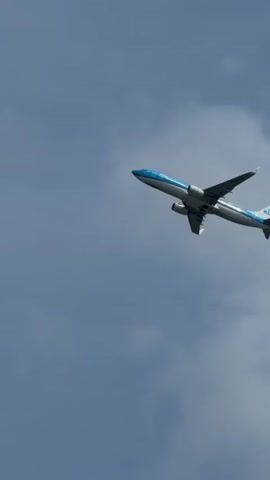 This is a close-up, low-angle shot of a KLM airplane in flight against a clear, pale blue sky. The aircraft is white with a distinctive blue stripe running along its fuselage, and the KLM logo is visible on the tail. The plane appears to be climbing or banking, with its wings tilted upwards. The landing gear is retracted.

The time of day appears to be daytime, given the brightness of the sky. The weather seems fair with no visible clouds or precipitation. The location context of Vijfhuizen, Netherlands, suggests the plane might be departing from or approaching Amsterdam Airport Schiphol (AMS).

The image focuses solely on the airplane and the sky, creating a sense of the vastness of the atmosphere and the powerful engineering of flight. There is no visible text on the fuselage or wings other than the airline's branding and the registration number "PH-EGX" on the tail. The overall mood is one of observation and perhaps awe at the sight of a large aircraft in motion.