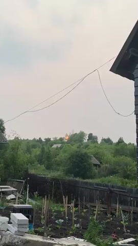 A video of a sunset behind trees and houses. The sky is hazy and the sun is a bright orange orb. There are power lines in the foreground.
