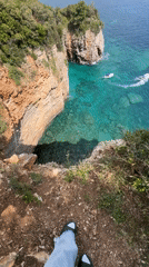 Clifftop visitor observes coastal scene with boat in Budva