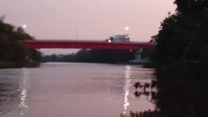 Red bridge over calm Kediri river at dusk, bus crossing