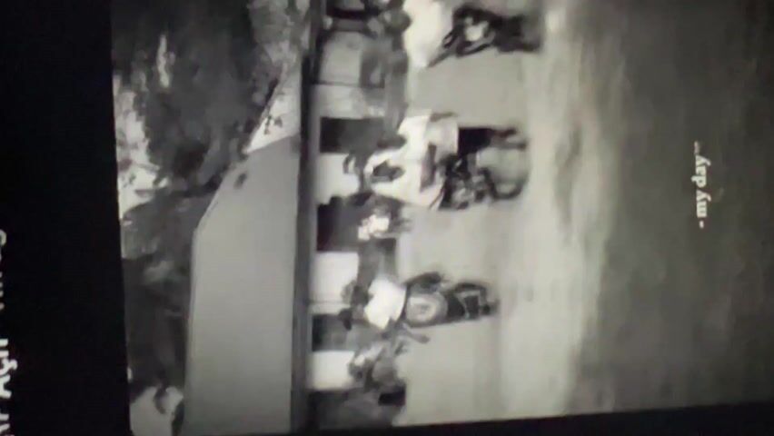 The video shows a black-and-white image of several people walking or standing in an outdoor setting. They are wearing light-colored shirts. The setting appears to be grassy with some trees or foliage in the background. The video transitions to a close-up of a man wearing a white t-shirt and a bandana or head covering with writing on it. He is lying down. The text "- my day" is visible on the screen. The scene is dark.