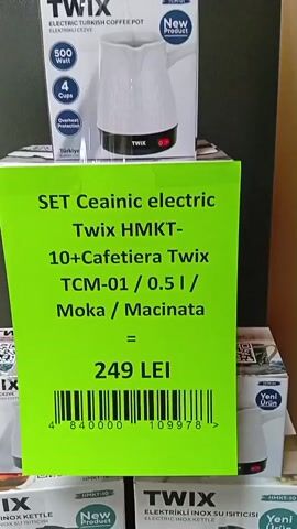 The video shows a display of TWIX brand electric kettles and coffee pots, likely in a retail store. The items are stacked in boxes, with a prominent green sign in the foreground advertising a set that includes a TWIX HMK T-10 coffee maker and a TCM-01 Moka pot for 249 LEI. The boxes show images of the products, their brand name, and some specifications like wattage and capacity. The overall lighting is dim, suggesting an indoor environment. There are no people visible in the video.