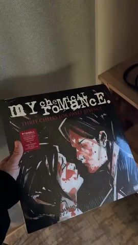 A person holds a vinyl record of My Chemical Romance's album "Three Cheers for Sweet Revenge". The front cover is displayed, followed by the back cover which lists the track titles. The video takes place indoors.