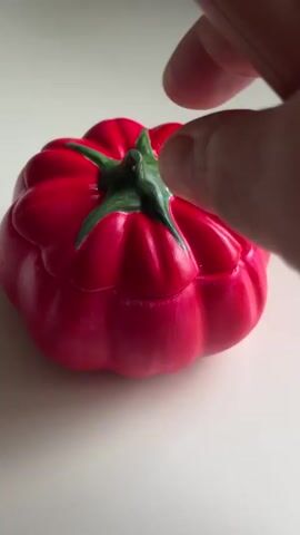 A hand is holding a lighter and is about to light a candle. The candle is in a red, pumpkin-shaped holder. The candle is white and has a wick. The background is a plain white surface.