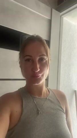 The video shows a woman in a close-up shot, likely a selfie. She is wearing a grey ribbed tank top and a silver necklace with a star pendant. Her hair is pulled back, and she has on light makeup. The background appears to be indoors, with a door or partition visible. The lighting suggests it might be daytime. The woman's expression is neutral, with a slight smile. There is no discernible text in the video. The context provided indicates the location is Zarichne, Ukraine, but this cannot be visually confirmed from the media alone.