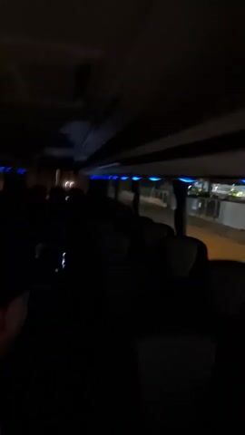 The video appears to have been taken inside a bus or similar vehicle at night. The camera is shaky and the lighting is poor, making it difficult to see clearly. The interior of the vehicle has blue LED strip lighting. The outside is visible through the window and shows blurred streetlights. Sounds of dogs are present.