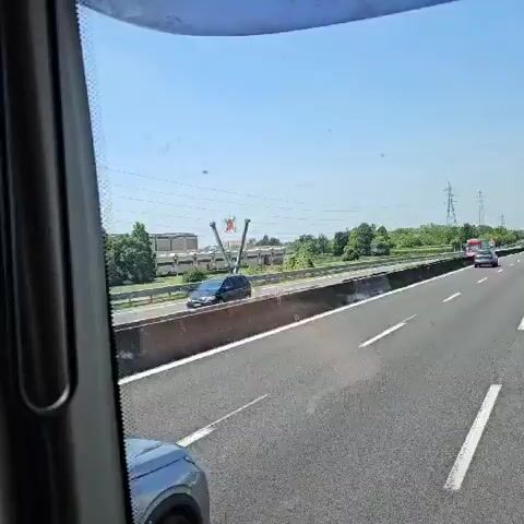 Here's a description of the video:

The video is shot from inside a moving vehicle, likely a bus or truck, traveling on a highway. The camera is pointed towards the passenger window, capturing the passing scenery. 

Visible outside are other cars and trucks moving on the highway. Adjacent to the highway, there's an area with grass and greenery. In the background, various buildings and structures can be seen. Notably, there's a structure with the large letters "XXL" on top.  Also observed is an SOS sign along the highway.