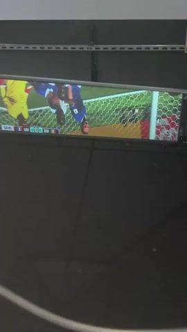 The video shows a projected image of a soccer game on a screen. The game appears to be between France and Senegal, with the score 0-0. The projection is reflected on a surface below, creating an inverted image. The environment appears to be outdoors, possibly under a canopy or awning, with visible structural elements above the projection screen.
