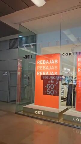 The video shows the storefront of a clothing store. The store is called Corte Fiel and Pedro del Hierro. The storefront has large glass windows displaying various signs and clothing items. The signs advertise sales, with discounts of -60%, -50%, and -70%. Inside the store, mannequins are dressed in clothes, and racks of clothing are visible. The store appears to be well-lit and organized. There are no people prominently featured in the video, and no specific actions are being taken. The environment is that of a retail store, likely in a mall or shopping center.