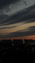 City skyline at dusk, clouds shifting from gray to vivid sunset