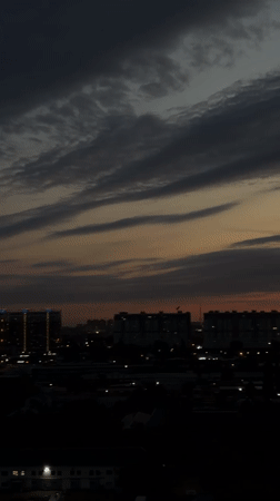 City skyline at dusk, clouds shifting from gray to vivid sunset