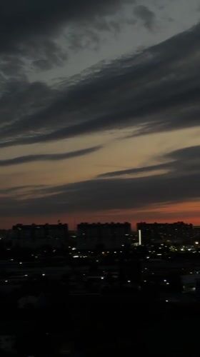 City skyline at dusk, clouds shifting from gray to vivid sunset