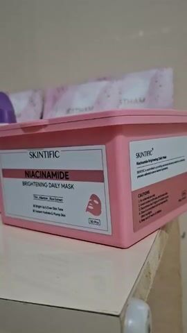 The video shows a collection of skincare products arranged on a white shelf. The items are positioned close together and include a pink box of Skintific Niacinamide Brightening Daily Masks, several bottles of micellar water (one is Wardah and another is The Originote Hyalurose Micellar Water), a white tube labeled “Somethinc TRIPLE CARE SUNSCREEN,” and two containers of cream. One cream is in a purple and pink container and says "emina bright glow" on the lid. The other cream is in a dark brown container with the brand name "TAZZI" written on it. In the background are some individual sheet masks. The items appear to be arranged against a plain, light-colored wall.