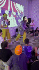 Women in yellow entertain children with music in purple-lit room