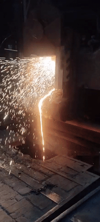Torch cutting molten metal, sparks flying in dark industrial setting