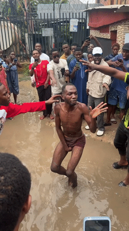 Crowd surrounds restrained person in muddy puddle, Ihiagwa, Nigeria